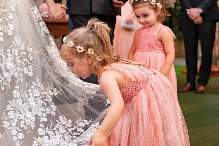 Linda fotografia de criança daminha ajeitando o vestido da noiva