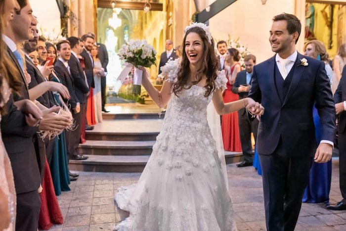 Foto fantástica de noiva feliz saindo da igreja após casar de mãos dadas com o noivo e padrinhos do lado
